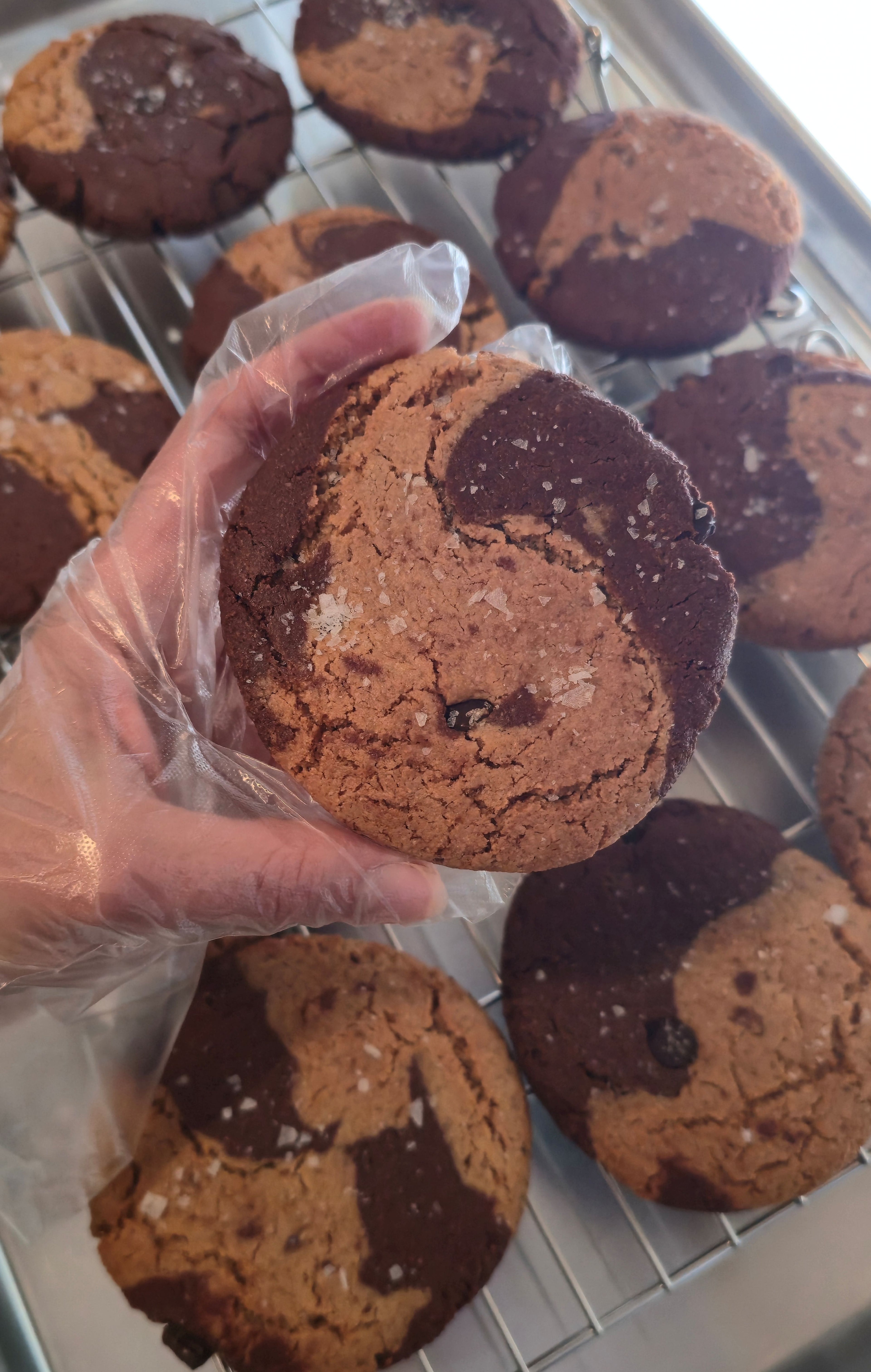 Hand holding a chocolate and peanut butter marble cookie with more cookies on a cooling rack in the background