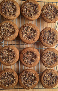 Twelve golden-brown cookies filled with peach preserves, and topped with rolled oats streusel on a metal cooling rack over a light wood surface.